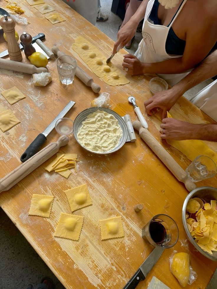 Hands shaping ravioli on a floured wooden table with rolling pins